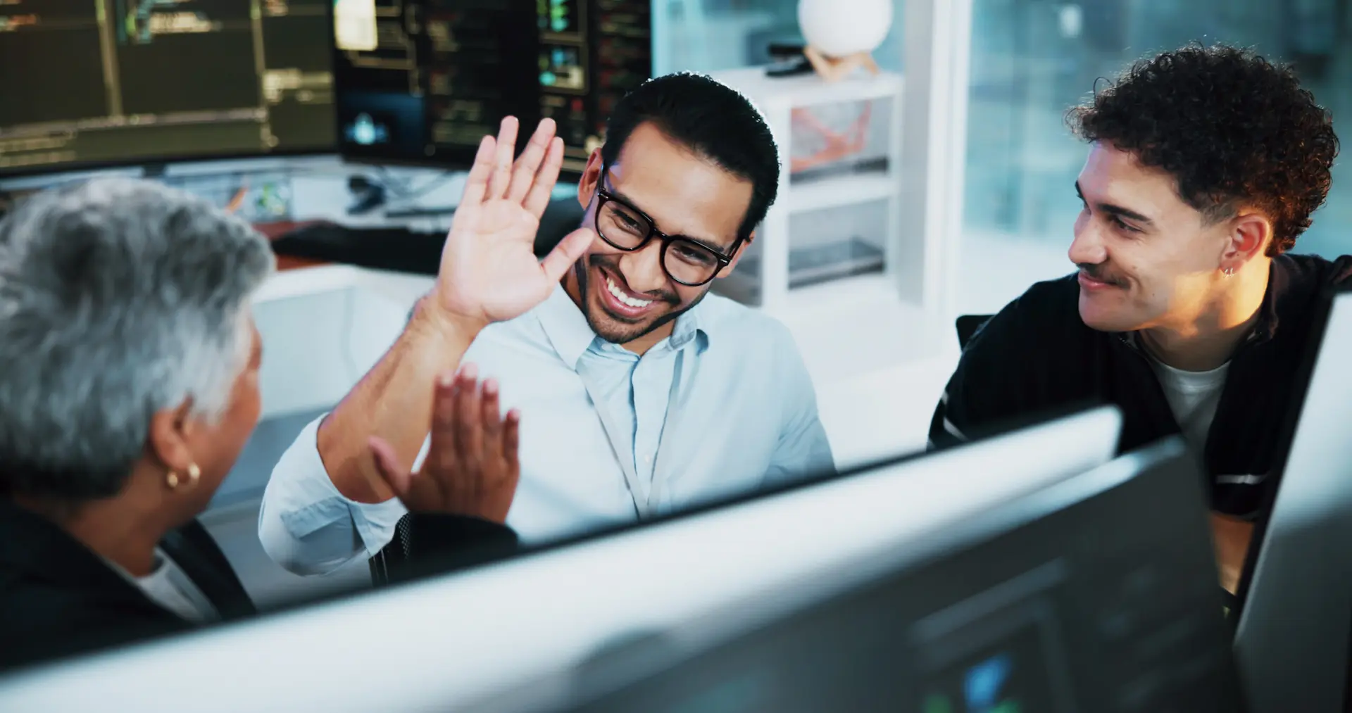 IT Consultant wearing glasses and a button up shirt high-fiving an older woman in front of computers